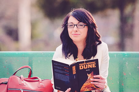 woman sitting on green metal bench reading Dune book during daytime thumbnail
