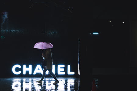 woman walking beside Chanel LED signage while holding umbrella during nighttime thumbnail