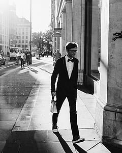 grayscale photo of man in suit walking near wall thumbnail