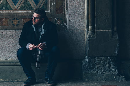 man sitting near wall while holding earbuds thumbnail