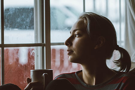 woman holding white ceramic mug staring outside thumbnail