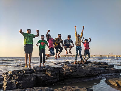 Boy Wearing Green Crew-neck Shirt Jumping from Black Stone on Seashore thumbnail