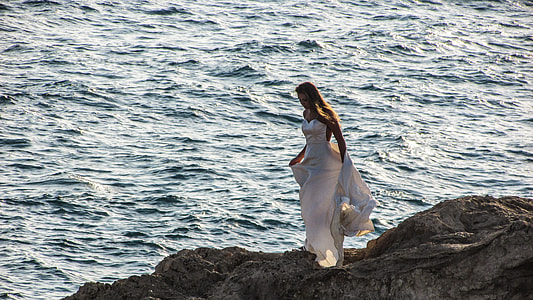 woman wearing white wedding dress on rock near body of water thumbnail