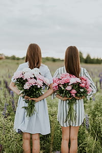 two woman holding pink flower bouquets standing on green grass field thumbnail