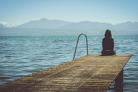 person sitting on wooden dock across body of water thumbnail
