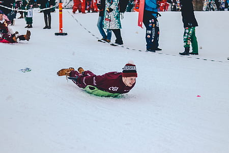 man in red shirt sliding on snow with green board during daytime thumbnail