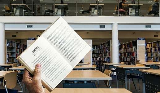 Photo illustration of book being held up in a library with empty desks thumbnail
