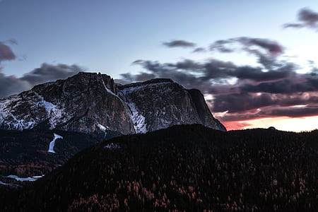 white and black rocky mountain with distance to forest under blue and white sky thumbnail