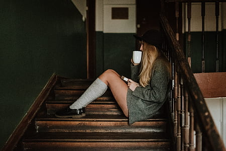 woman holding white ceramic mug sitting on stairs thumbnail