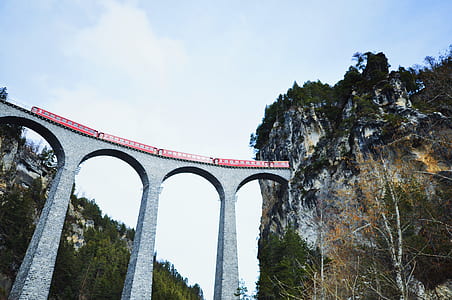 low-angle photography of red train passing on gray concrete train rail connected to mountain tunnel during daytime thumbnail