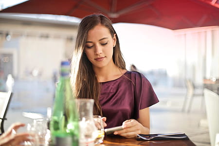 A young blonde woman wearing a purple red dress looking at her mobile phone screen at a restaurant thumbnail