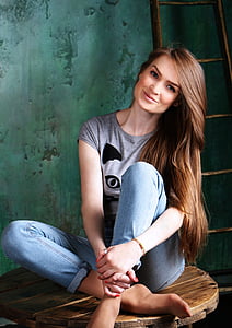 woman in grey top and blue jeans sitting on brown spool table near brown ladder thumbnail