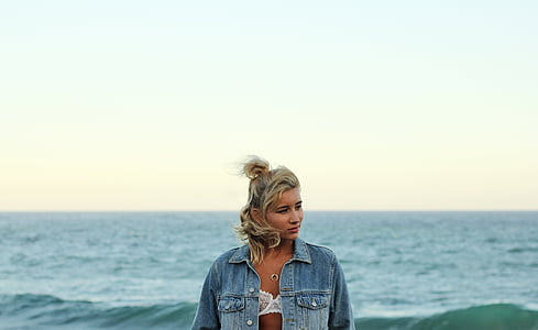 woman wearing white floral brassiere and blue denim jacket near ocean during daytime thumbnail