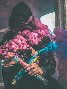 person in black hoodie holding blue and purple rainbow smoke makers thumbnail