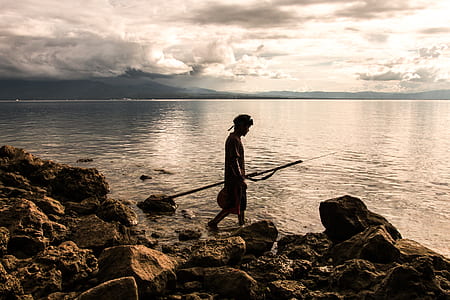 Person Holding Spear Beside Body of Water thumbnail