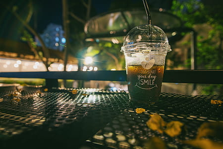 Clear Plastic Disposable Cup With Straw Half-filled With Juice on Metal Table thumbnail