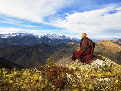 monk sitting on the cliff on the mountain under the blue sky during daytime thumbnail