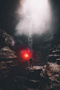 person holding red light inside cave with waterfall thumbnail