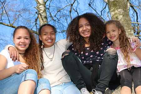 four girl sits on rock behind bare tree at daytime thumbnail