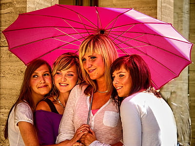 four women wearing clothes standing under pink umbrella thumbnail