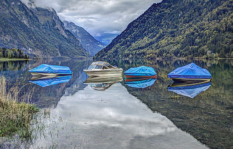 reflection of four speedboats floating on body of water with mountain background thumbnail