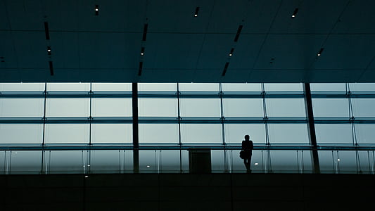 silhouette photograph of man standing while leaning on glass building barricade thumbnail