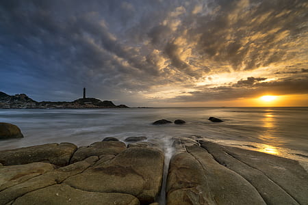 rock monolith beside body of water during sunrise thumbnail
