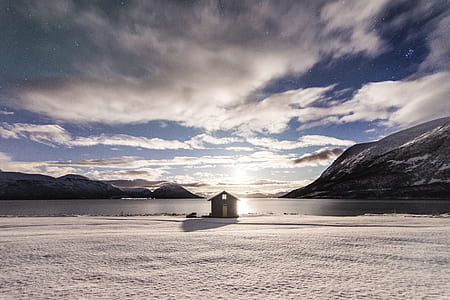silhouette of brown wooden shed near large body of water surrounded by mountains thumbnail