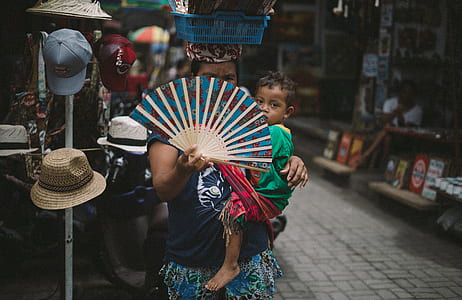 selective focus photography of woman carrying boy and holding hand fan thumbnail