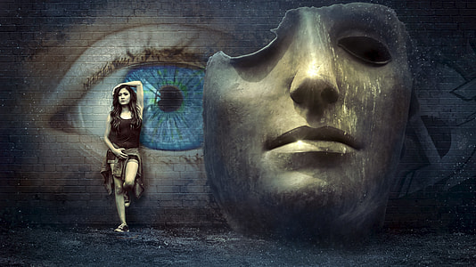 woman in black tanktop near gray and blue wall with eye and mask graffiti photography thumbnail