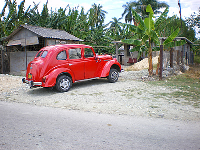 classic red vehicle parked near house and banana trees thumbnail