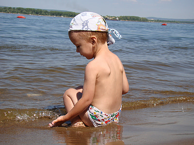 boy sitting on brown sand near the water at daytime thumbnail