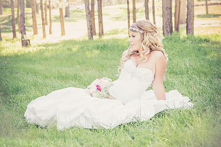 woman wearing white sweetheart neckline wedding dress sitting on green grass during daytime thumbnail
