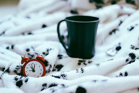 green ceramic mug beside red alarm clock on white and black textile closeup photo thumbnail