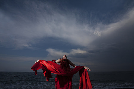 woman in red sleeveless dress and scarf bending near ocean thumbnail