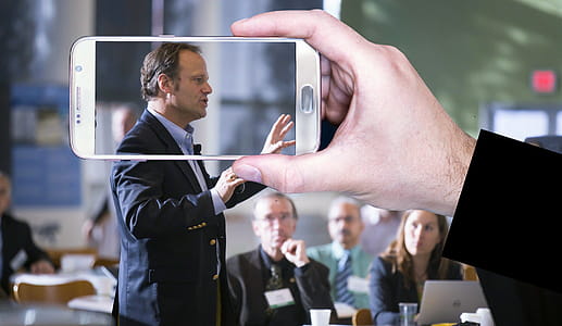 Photo illustration of taking a video or photo of a person speaking in public. thumbnail