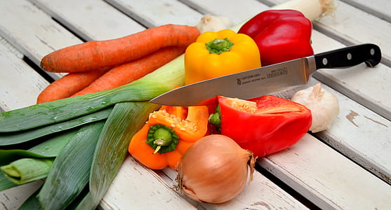red and yellow bell peppers carrots and onion with black handle kitchen knife thumbnail