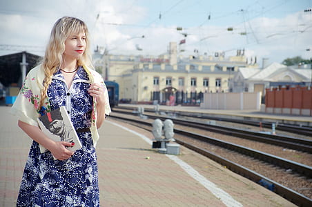 woman wearing floral dress holding male portrait standing beside train rails during daytime thumbnail