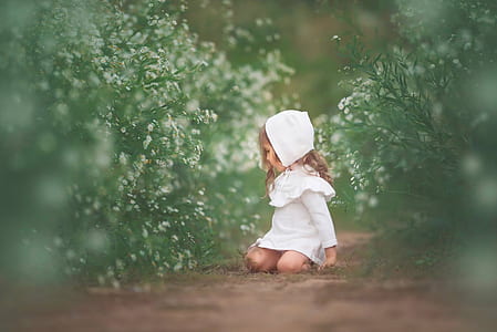selective focus photography of girl wearing white dress lying between green leaf plants at daytime thumbnail