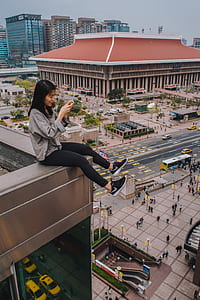 woman sitting on the edge of building while holding phone thumbnail