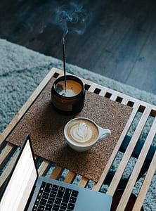 cappuccino filled white cup beside brown jar with lit incense stick and MacBook Pro thumbnail