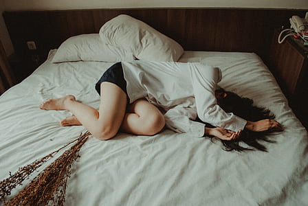 woman wearing long-sleeved shirt and black short shorts lying on white covered bed thumbnail