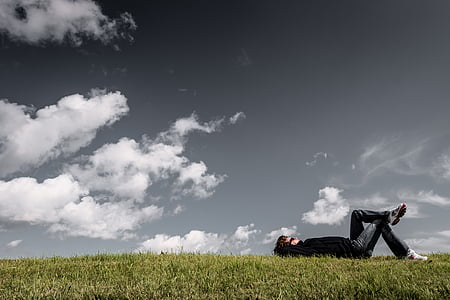 man lying on green grass field under cloudy sky thumbnail