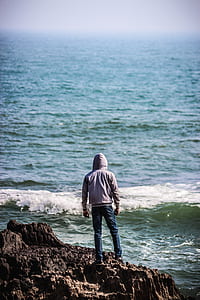 person standing on rock beside body of water thumbnail