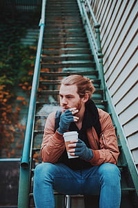 person sitting on stair holding coffee cup while smoking thumbnail