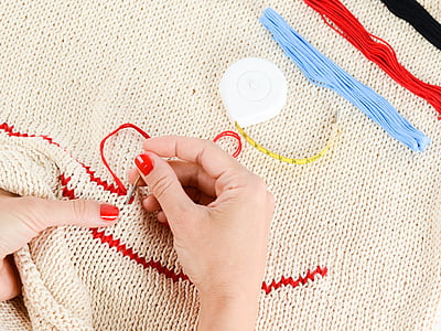 person sewing on beige knit textile with red thread thumbnail