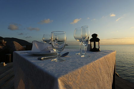 four empty wine glasses on white tablecloth near body of water at golden hour thumbnail
