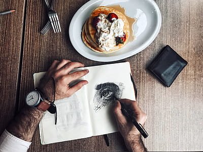 person sketching eyes beside pancakes on plate and wallet thumbnail