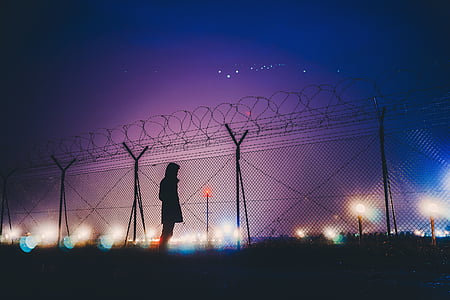 silhouette photograph of person standing beside link fence thumbnail