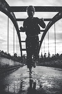 grayscale photography of woman jogging on bridge thumbnail